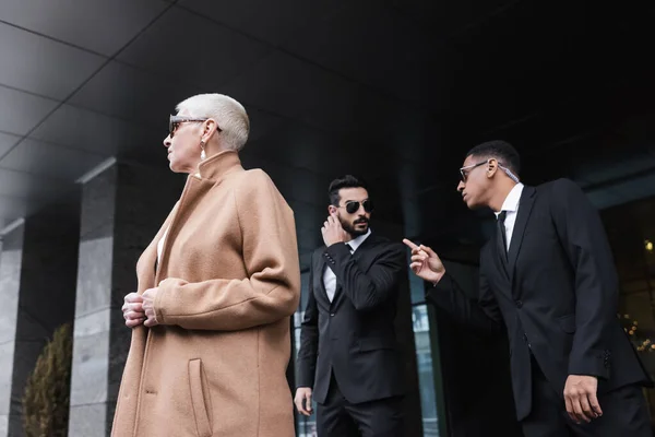 African american bodyguard pointing with finger near bi-racial colleague and senior business lady outdoors — Stock Photo