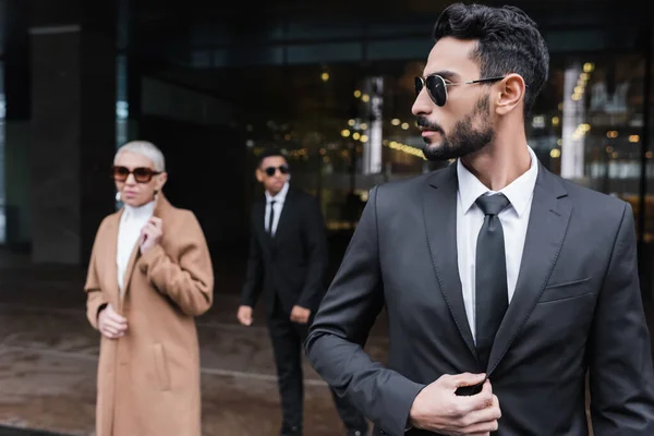 Guardaespaldas bi-racial mirando hacia otro lado cerca de la mujer de negocios senior y el hombre de seguridad afroamericano al aire libre - foto de stock