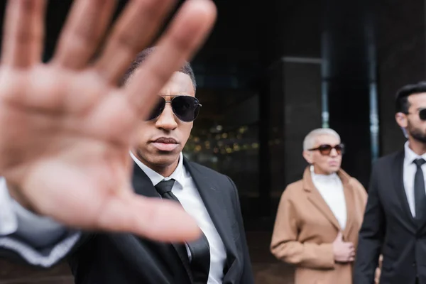 Uomo di sicurezza razza mista mostrando gesto stop vicino anziana donna d'affari e guardia del corpo afroamericana — Foto stock