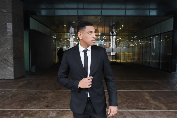 African american security man in formal wear looking away near entrance of hotel outdoors — Stock Photo