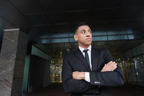 African american guard looking away while standing with crossed arms near hotel entrance — Stock Photo