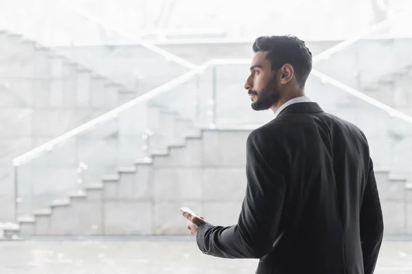 Homme de sécurité bi-raciale avec smartphone regardant loin dans le hall de l'hôtel flou — Photo de stock