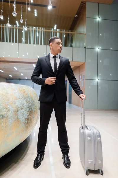 Vue pleine longueur de garde afro-américain avec valise regardant loin près de la réception de l'hôtel — Photo de stock