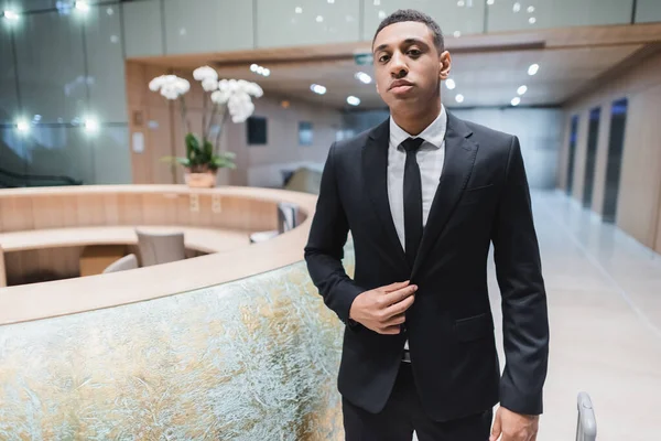 Homem de segurança afro-americano de terno preto olhando para a câmera no lobby do hotel — Fotografia de Stock