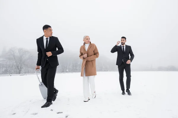 Afrikanisch-amerikanischer Sicherheitsmann trägt Koffer in der Nähe von Geschäftsfrau und Leibwächter zweier Rassen auf schneebedecktem Feld — Stockfoto