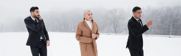 Afro-américain homme de sécurité pointant direction près mature femme d'affaires et garde bi-raciale sur le champ d'hiver, bannière — Photo de stock