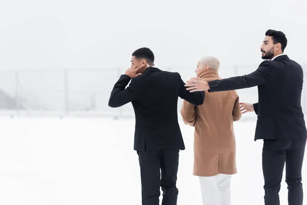 Back view of mature businesswoman walking across winter field under protection of interracial bodyguards — Stock Photo