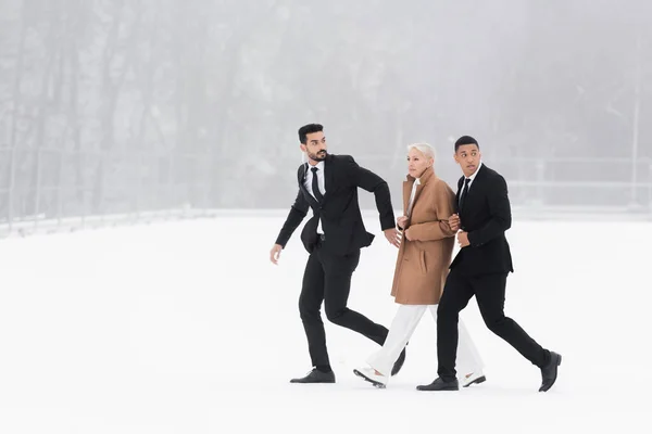 Full length view of multiethnic bodyguards protecting mature businesswoman walking on winter field — Stock Photo