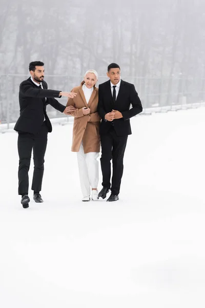 Homem de segurança bi-racial apontando direção perto de empresária sênior e guarda-costas afro-americana no campo de inverno — Fotografia de Stock