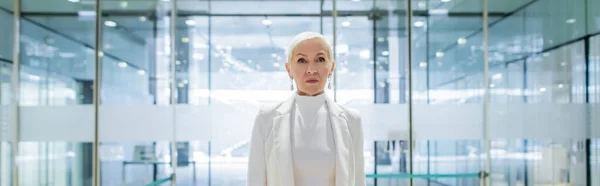 Senior businesswoman in white clothes standing in hotel near entrance, banner — Stock Photo