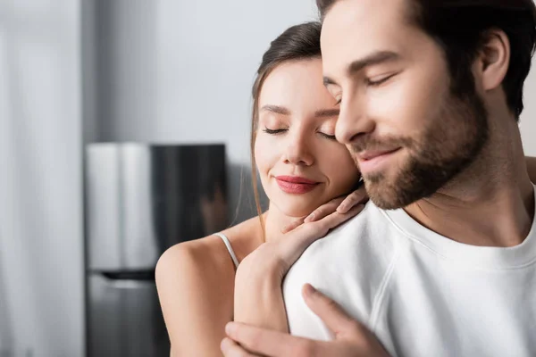 Cheerful woman hugging blurred and bearded boyfriend with closed eyes — Stock Photo