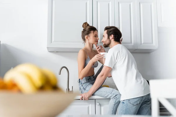 Homme barbu séduire jeune femme en soutien-gorge avec tasse dans la cuisine — Photo de stock