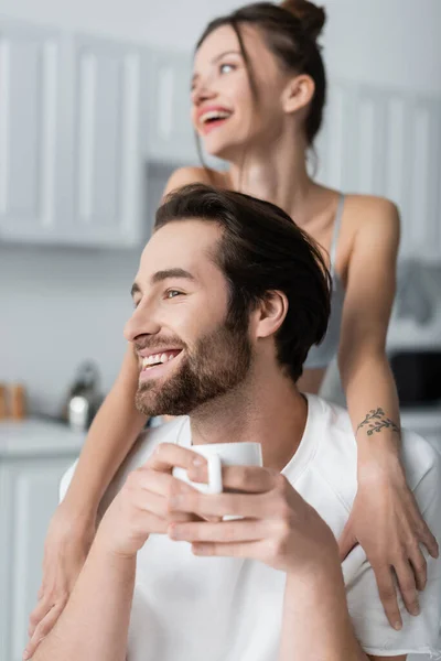 Verschwommene und tätowierte Frau umarmt glücklichen Mann mit Tasse — Stockfoto