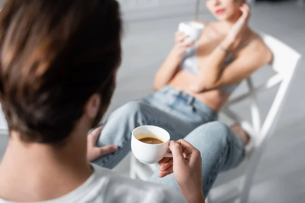 Blurred man holding cup of coffee near girlfriend in kitchen — Stock Photo