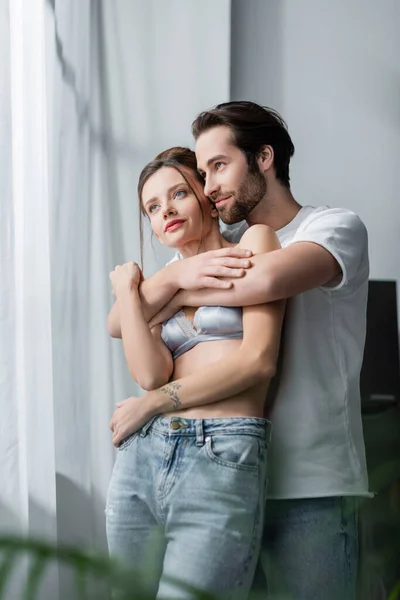 Pleased bearded man hugging tattooed girlfriend in bra — Stock Photo