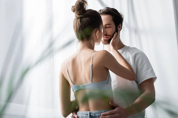 Vue arrière de la femme en soutien-gorge et homme barbu étreignant à la maison — Photo de stock