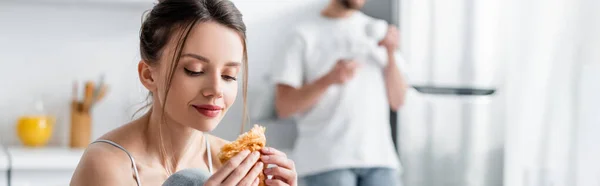 Jeune femme tenant croissant près de flou homme sur fond, bannière — Photo de stock