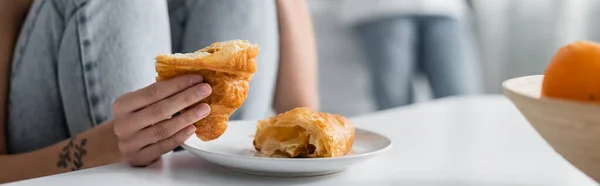 Cropped view of tattooed woman holding croissant, banner — Stock Photo