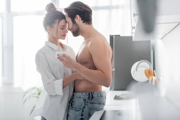 Hombre sin camisa sosteniendo taza y abrazando con sensual joven mujer - foto de stock