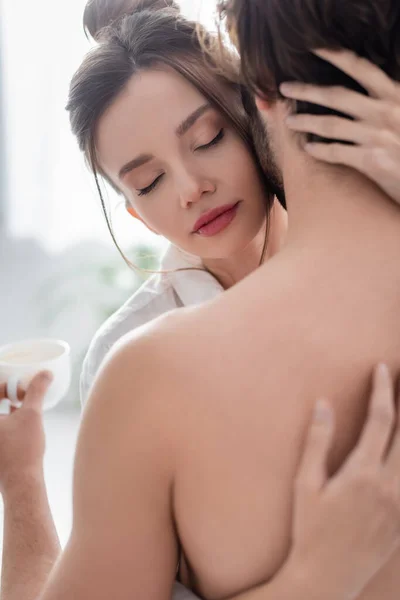 Young woman hugging shirtless man holding cup — Stock Photo