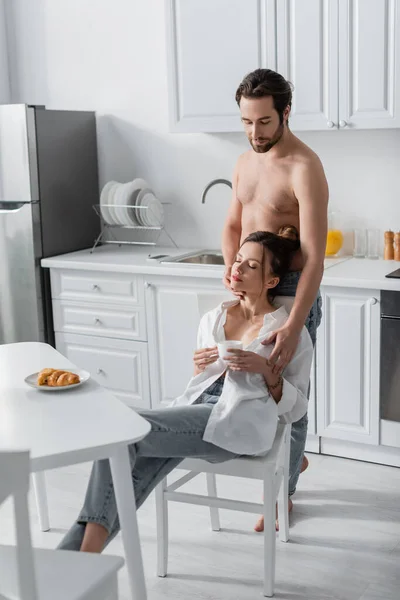 Hombre sin camisa abrazando a mujer joven con taza de café - foto de stock