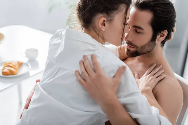 Femme passionnée embrassant homme barbu et torse nu dans la cuisine — Photo de stock