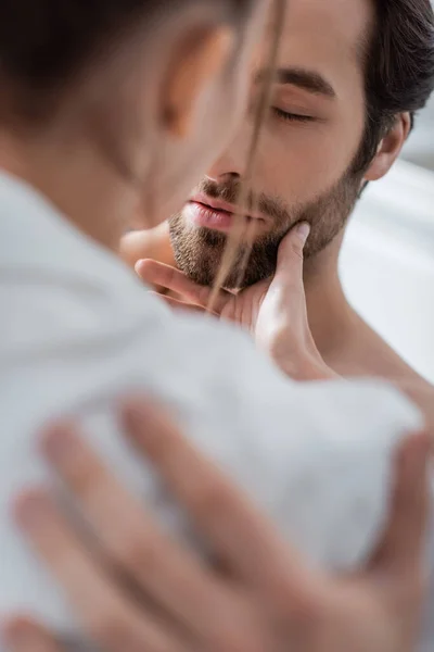 Mujer borrosa tocando la cara del novio barbudo con los ojos cerrados - foto de stock