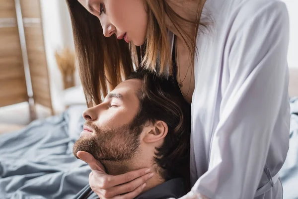 Young woman in silk robe hugging bearded boyfriend with closed eyes — Stock Photo