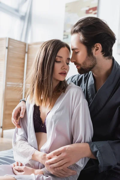 Bearded man looking at pretty girlfriend in silk robe — Stock Photo