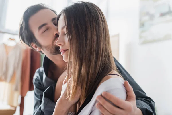 Giovane uomo con gli occhi chiusi baciare guancia di bella fidanzata in vestaglia di seta — Foto stock