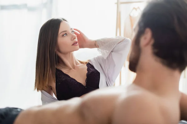 Tattooed young woman in silk robe and black bra near blurred shirtless man — Stock Photo