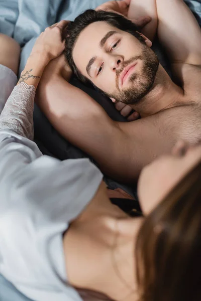 Vista de ángulo alto de la mujer borrosa y tatuada cerca del hombre sin camisa en el dormitorio - foto de stock