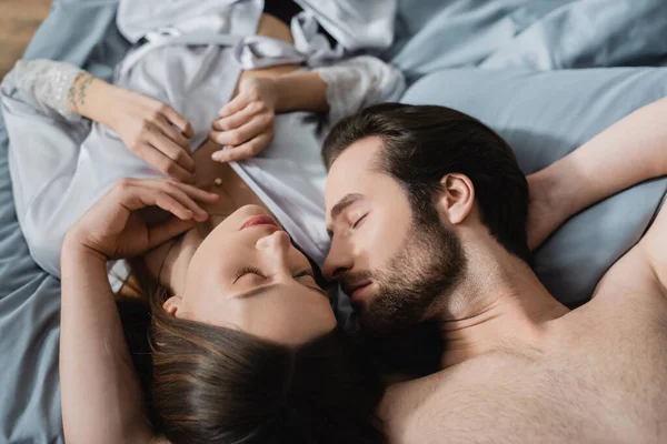 Hochwinkelaufnahme einer tätowierten Frau, die mit einem Mann ohne Hemd auf dem Bett liegt — Stockfoto