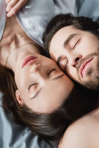 Вид сверху молодой женщины и мужчины с закрытыми глазами, лежащих на кровати — стоковое фото