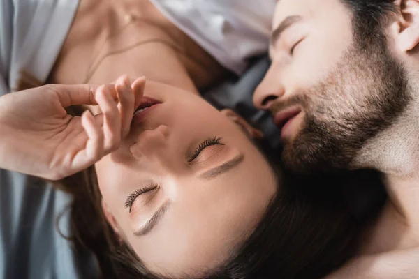 Vista dall'alto di giovane donna e uomo barbuto con gli occhi chiusi sdraiati sul letto — Foto stock