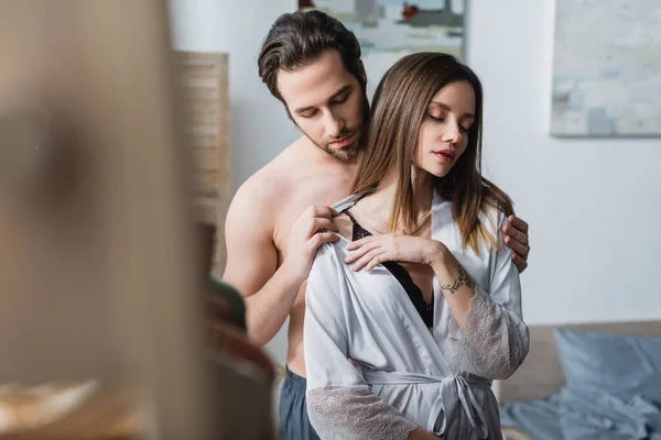 Shirtless man taking off silk robe on tattooed girlfriend — Stock Photo