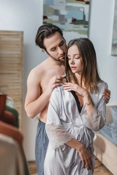 Shirtless man undressing tattooed girlfriend in silk robe — Stock Photo