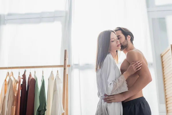 Homem sem camisa beijando jovem mulher em roupão de seda — Fotografia de Stock