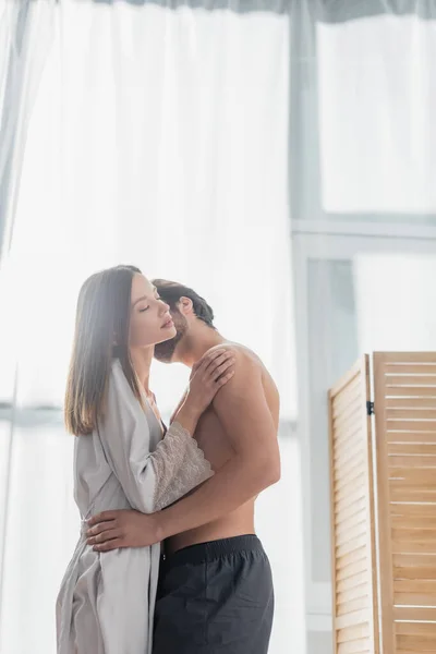 Без рубашки мужчина целует красивую молодую женщину в шелковом халате — стоковое фото