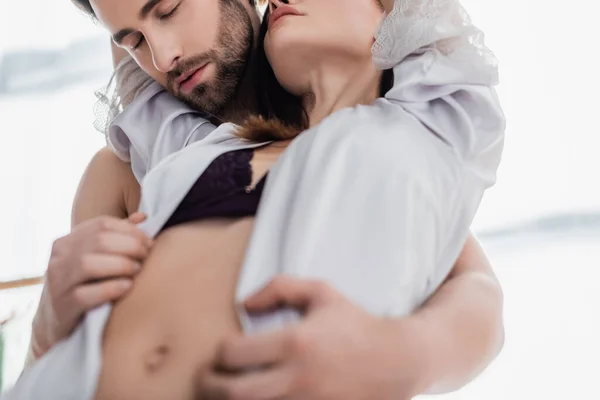 Hombre barbudo seduciendo a mujer joven en ropa interior y bata de seda - foto de stock