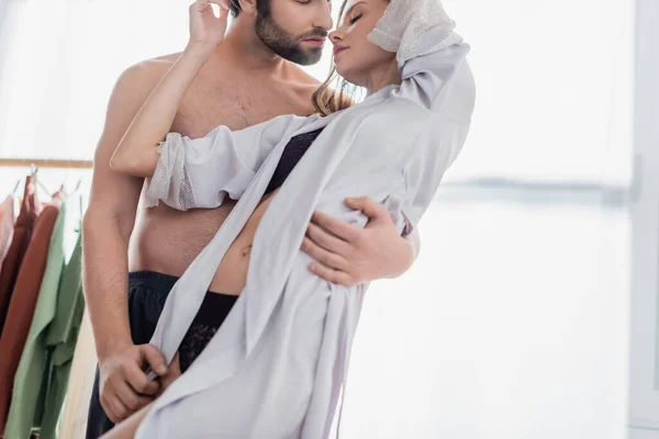 Hombre barbudo abrazando a mujer joven en ropa interior y bata de seda - foto de stock
