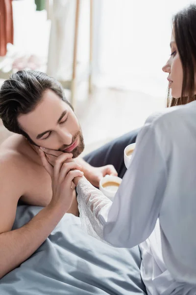 Young woman touching face of bearded man and holding cup — Stock Photo