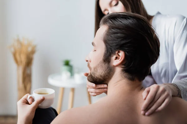 Blurred woman with tattoo hugging bearded man with cup of coffee — Stock Photo