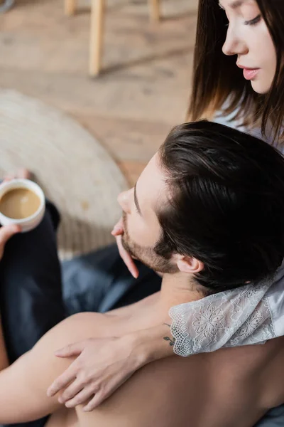 Vista de ángulo alto de la joven mujer tatuada seduciendo a hombre con taza de café - foto de stock