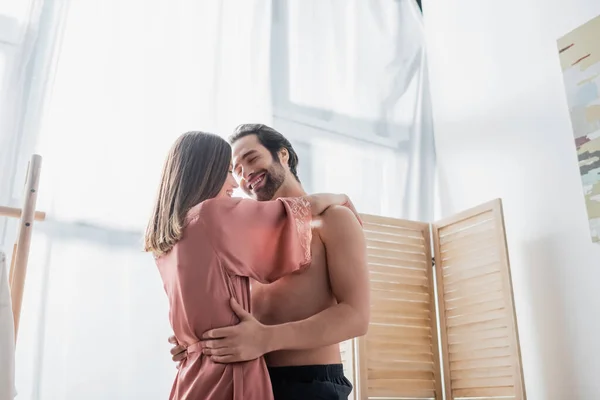 Barbudo y alegre hombre abrazando feliz novia en rosa bata de seda - foto de stock