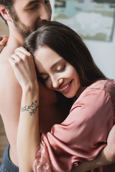 Heureuse femme tatouée en soie rose robe étreignant homme barbu — Photo de stock