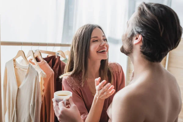 Щасливий чоловік тримає чашку кави біля веселої жінки, що сміється вдома — стокове фото