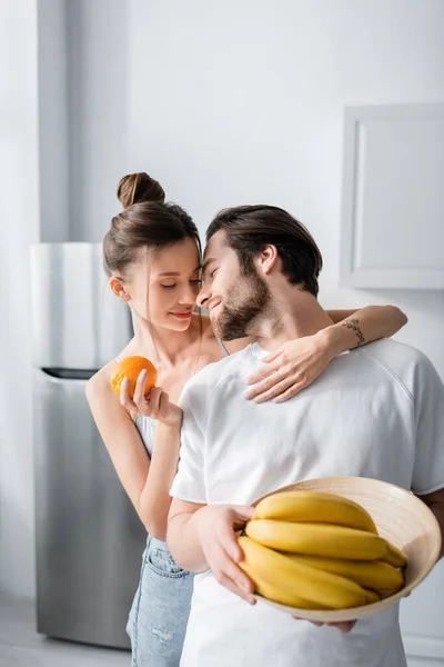 Tätowierte Frau umarmt Mann mit Schale mit Bananen — Stockfoto