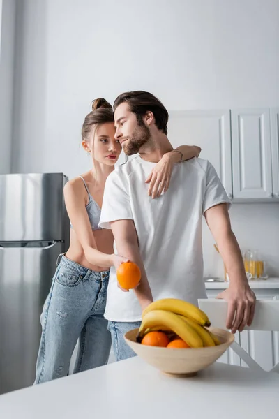 Tätowierte Frau umarmt Mann und hält frische Orange — Stockfoto