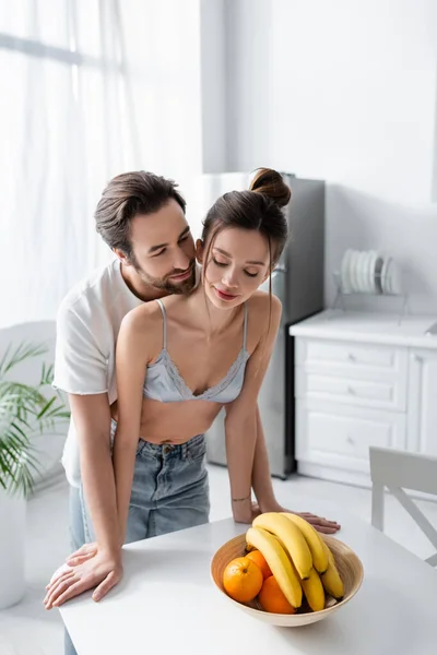 Bärtiger Mann steht mit Frau in BH und Jeans neben Früchten in Schale — Stockfoto